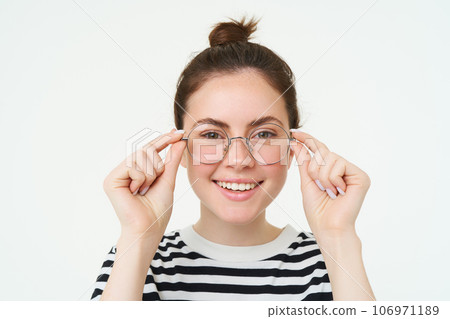 Close up portrait of beautiful woman, trying on new glasses, buying eyewear, smiling and looking happy, standing over white background 106971189