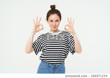 No problem, excellent choice. Smiling, confident young woman, showing okay, ok sign, zero gesture, recommends product, stands over white background No problem, excellent choice. Smiling, confident young woman, showing okay, ok sign, zero gesture, recommends product, stands over white background 106971254