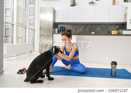 Portrait of smiling, beautiful woman doing sports, workout from home with her black dog, doing sports in living room 106971287