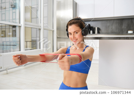 Focused sportswoman workout at home, using elastic resistance band on arms, stretching exercises in living room, aerobics training 106971344