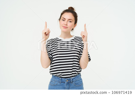 Advertising and lifestyle concept. Smiling cute woman pointing fingers up, showing advertisement, banner on top, standing over white background Advertising and lifestyle concept. Smiling cute woman pointing fingers up, showing advertisement, banner on top, standing over white background 106971419