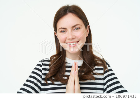 Portrait of young woman expresses her gratitude, shows thank you, namaste gesture, holding hands clasped together near chest and smiling, standing over white background Portrait of young woman expresses her gratitude, shows thank you, namaste gesture, holding hands clasped together near chest and smiling, standing over white background 106971435