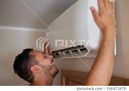 handsome man suffering from heat under air conditioner at home 106971678