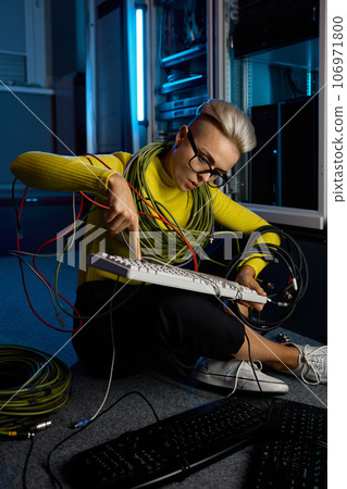 Young woman IT technician wrapped in wire repairing keyboard 106971800