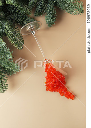 Red caviar splashed out of a glass wine glass. Spruce branches in the background. Salmon caviar. Delicacies. A festive snack. A useful omega. 106972089
