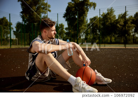 Young adult basketball player rest on urban street court 106972092