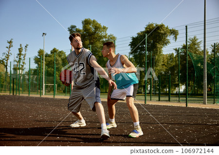 Active young men playing basketball on street court 106972144