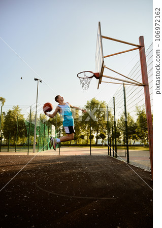 Teenager boy aiming into basketball hoop playing on playground 106972162