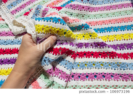 A hand touching a soft colored knitted blanket in the bright light of the sun. 106973196