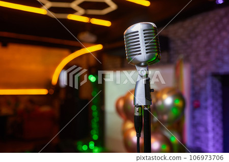 Retro Microphones on front stage in pub bar or restaurant. Classic sing a song in evening and night show concert light bokeh background. Retro Microphones on front stage in pub bar or restaurant. Classic sing a song in evening and night show concert light bokeh background. 106973706