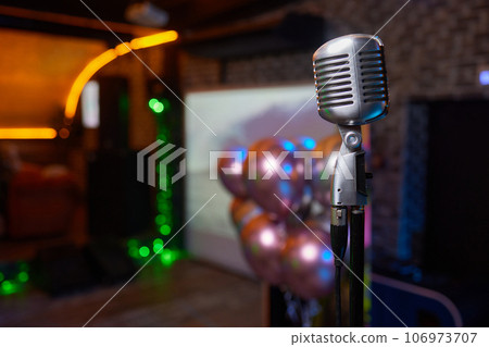 Retro Microphones on front stage in pub bar or restaurant. Classic sing a song in evening and night show concert light bokeh background. Retro Microphones on front stage in pub bar or restaurant. Classic sing a song in evening and night show concert light bokeh background. 106973707