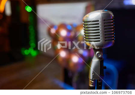 Retro Microphones on front stage in pub bar or restaurant. Classic sing a song in evening and night show concert light bokeh background. Retro Microphones on front stage in pub bar or restaurant. Classic sing a song in evening and night show concert light bokeh background. 106973708