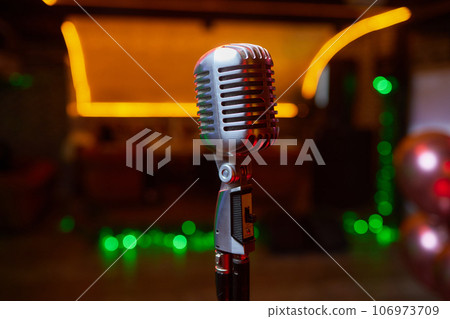 Retro Microphones on front stage in pub bar or restaurant. Classic sing a song in evening and night show concert light bokeh background. Retro Microphones on front stage in pub bar or restaurant. Classic sing a song in evening and night show concert light bokeh background. 106973709