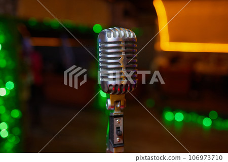 Retro Microphones on front stage in pub bar or restaurant. Classic sing a song in evening and night show concert light bokeh background. Retro Microphones on front stage in pub bar or restaurant. Classic sing a song in evening and night show concert light bokeh background. 106973710