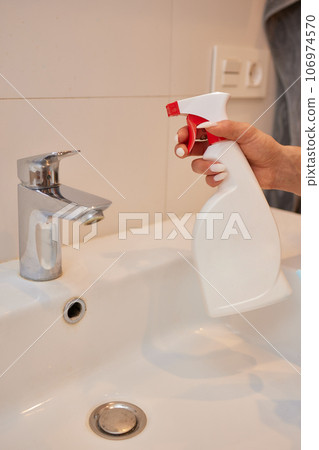 Cropped image of beautiful young woman using a duster and a detergent while cleaning sink and tap in bathroom. Cropped image of beautiful young woman using a duster and a detergent while cleaning sink and tap in bathroom. 106974570