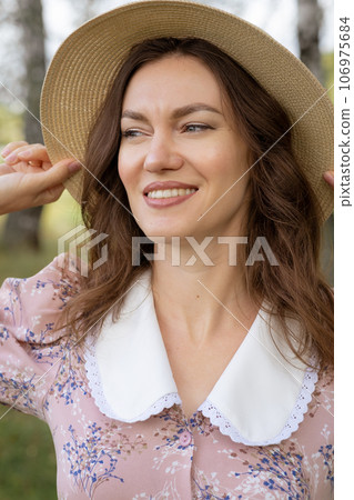 A young beautiful woman in a dress and holding a hat with her hands and reading a book in nature. Romantic and vintage photo of a beautiful girl. Reading and relaxation 106975684
