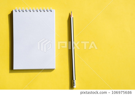 Open notepad and pencil or pen on yellow background. Composition of writing to-dos for the day. The notebook lies on a plain background with space for writing.  106975686