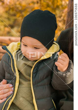 Cute little asian boy stands outdoors. Happy child walking in autumn park. Toddler baby boy wears trendy jacket and hat. Autumn fashion. Stylish child outside. 106975688