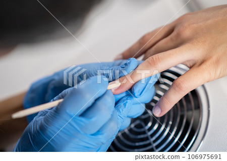 Nail care procedure in a beauty salon. Female hands and tools for manicure, process of performing manicure in beauty salon. Concept spa body care. Gloved hands of a skilled manicurist cutting cuticles Nail care procedure in a beauty salon. Female hands and tools for manicure, process of performing manicure in beauty salon. Concept spa body care. Gloved hands of a skilled manicurist cutting cuticles 106975691