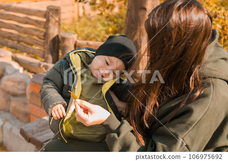 Cute little asian boy with mother outdoors. Happy child walking in autumn park. Toddler baby boy wears trendy jacket and hat. Autumn fashion. Stylish child outside. 106975692