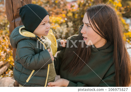 Cute little asian boy stands with mother outdoors. Happy child walking in autumn park. Toddler baby boy wears trendy jacket and hat. Autumn fashion. Stylish child outside. Cute little asian boy stands with mother outdoors. Happy child walking in autumn park. Toddler baby boy wears trendy jacket and hat. Autumn fashion. Stylish child outside. 106975827