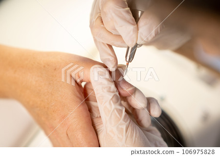 Nail care procedure in a beauty salon. Female hands and tools for manicure, process of performing manicure in beauty salon. Gloved hands of a skilled manicurist cutting cuticles. Concept spa body care Nail care procedure in a beauty salon. Female hands and tools for manicure, process of performing manicure in beauty salon. Gloved hands of a skilled manicurist cutting cuticles. Concept spa body care 106975828