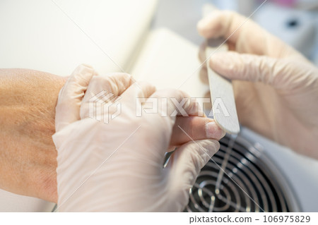 Nail care procedure in a beauty salon. Female hands and tools for manicure, process of performing manicure in beauty salon. Gloved hands of a skilled manicurist cutting cuticles. Concept spa body care Nail care procedure in a beauty salon. Female hands and tools for manicure, process of performing manicure in beauty salon. Gloved hands of a skilled manicurist cutting cuticles. Concept spa body care 106975829