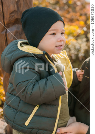 Cute little asian boy stands with mother outdoors. Happy child walking in autumn park. Toddler baby boy wears trendy jacket and hat. Autumn fashion. Stylish child outside. Cute little asian boy stands with mother outdoors. Happy child walking in autumn park. Toddler baby boy wears trendy jacket and hat. Autumn fashion. Stylish child outside. 106975830