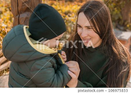 Cute little asian boy stands with mother outdoors. Happy child walking in autumn park. Toddler baby boy wears trendy jacket and hat. Autumn fashion. Stylish child outside. Cute little asian boy stands with mother outdoors. Happy child walking in autumn park. Toddler baby boy wears trendy jacket and hat. Autumn fashion. Stylish child outside. 106975833