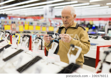 Elderly man buys a modern digital tablet in the showroom of the store Elderly man buys a modern digital tablet in the showroom of the store 106976011
