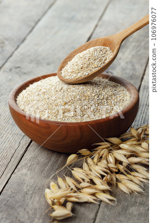 closeup of oat bran in bowl and in spoon with dry ears near on table 106976077