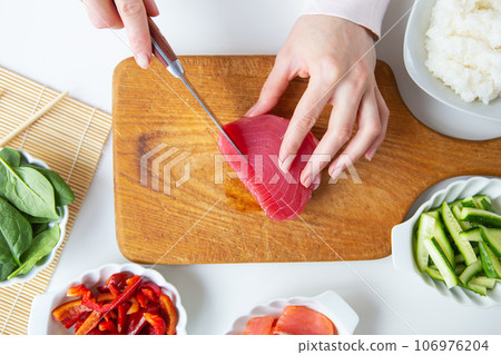 In the process of making sushi, preparing all the ingredients for sushi, the girl cuts the tuna. View from above. 106976204