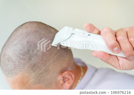 The hairdresser shaves the client's head with a white trimmer. Hairdressing salon, personal care. 106976216