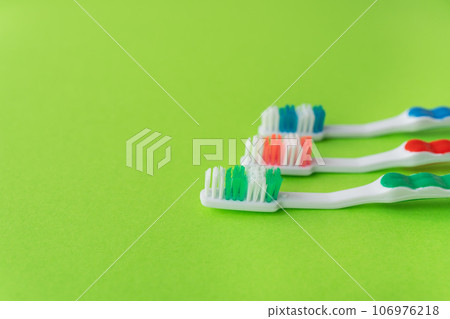 Three multi-colored toothbrushes on a light green background. Oral care concept. Place for inscriptions. Three multi-colored toothbrushes on a light green background. Oral care concept. Place for inscriptions. 106976218