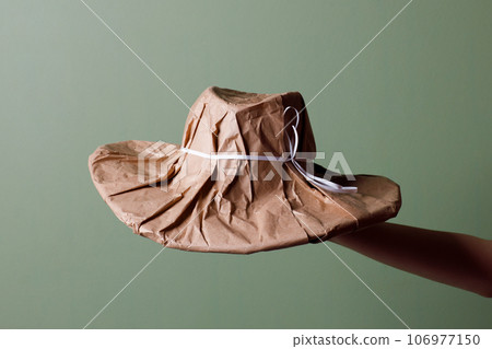 Female hand holds a brand new hat wrapped in rustic beige craft paper. Black Friday shopping concept. Female hand holds a brand new hat wrapped in rustic beige craft paper. Black Friday shopping concept. 106977150