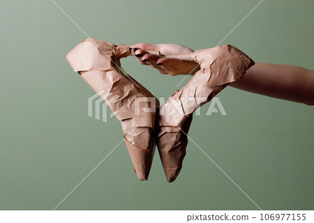 Female hand holds a brand new high heeled shoes wrapped in rustic beige craft paper. Black Friday shopping concept. Female hand holds a brand new high heeled shoes wrapped in rustic beige craft paper. Black Friday shopping concept. 106977155
