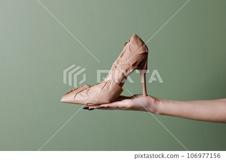 Female hand holds a brand new high heels shoes wrapped in rustic beige craft paper. Black Friday shopping concept. Female hand holds a brand new high heels shoes wrapped in rustic beige craft paper. Black Friday shopping concept. 106977156