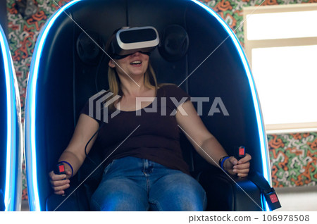 Virtual reality attraction, virtual glasses and entertainment in playrooms for children. A woman sits in a 5d neon chair. 106978508