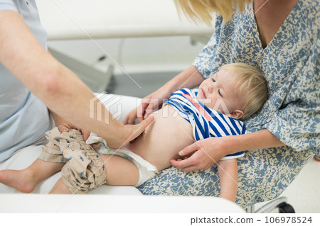 Infant baby boy child being examined by his pediatrician doctor during a standard medical checkup in presence and comfort of his mother. National public health and childs care care koncept 106978524