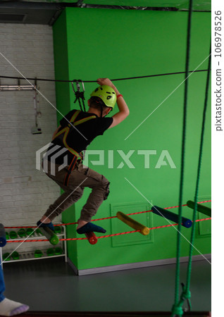 The boy actively and attentively passes the ropeway in the playroom. 106978526