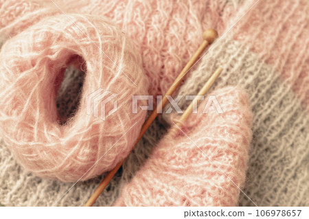 Yarn and knitting needles, top view. Grey and pink wool thread with needles. Knitting crochet. Knitted pattern. Needlework concept. Handmade pullover. Cozy warm clothing. Creativity and hobby.  106978657