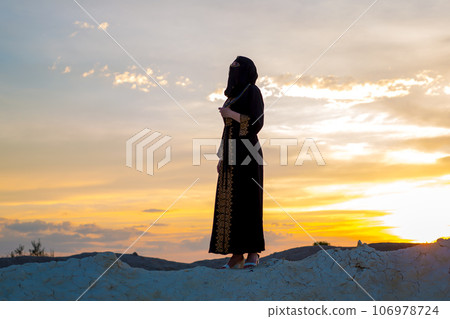 An Islamic woman prays while standing on a mountain at sunset. Religious tradition evening prayer 106978724