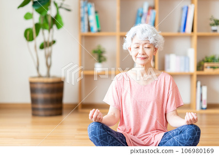 一位老年婦女在客廳裡做瑜伽。 一位老年婦女在客廳裡做瑜伽。 106980169