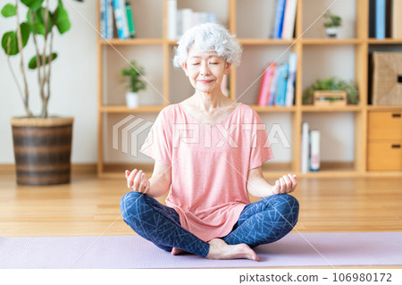 一位老年婦女在客廳裡做瑜伽。 一位老年婦女在客廳裡做瑜伽。 106980172