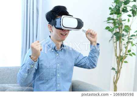 A young man in casual clothes wearing VR goggles 106980598