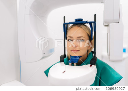 Front view of young female patient standing in dental x-ray machine for dental radiography in modern in dentistry clinic. Concept of dentistry, medicine, healthcare, jaw scanning. 106980927