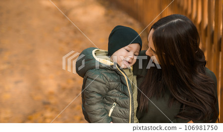 Cute little asian boy stands with mother outdoors copy space. Happy child walking in autumn park. Toddler baby boy wears trendy jacket and hat. Autumn fashion. Stylish child outside. 106981750