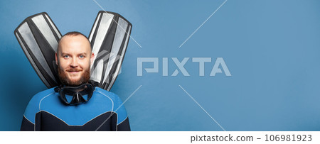 Closeup portrait of handsome diver diving man with flippers against blue studio wall background Closeup portrait of handsome diver diving man with flippers against blue studio wall background 106981923