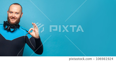 Closeup portrait of happy diver diving guy showing okay against colorful blue studio wall background Closeup portrait of happy diver diving guy showing okay against colorful blue studio wall background 106981924