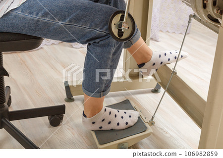 Female feet on the pedal of a sewing machine, motor 106982859